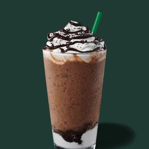 there is a drink with whipped cream and chocolate on top in a glass, next to a green background