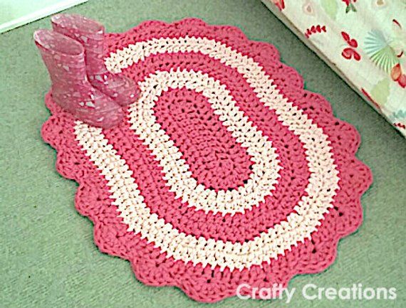 a pink and white crocheted rug on the floor next to a bed with a pillow