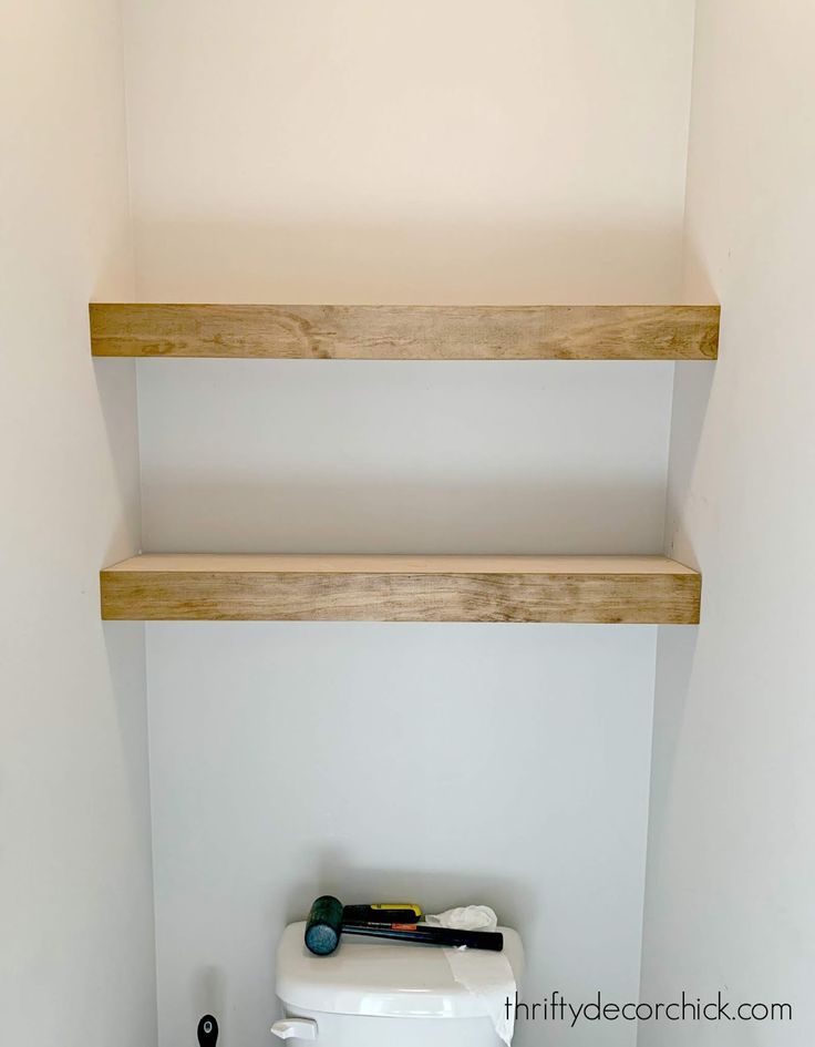 a toilet in a bathroom with two shelves above it