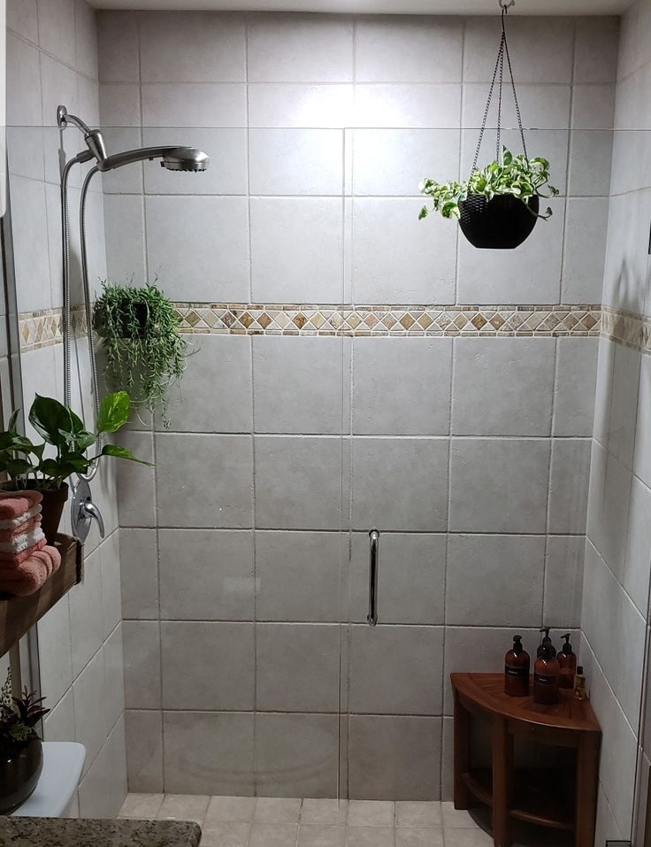 a white tiled shower with plants hanging from it's hooks and two potted plants on the wall