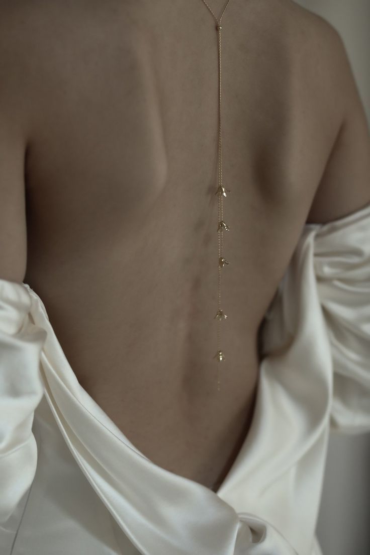 the back of a woman's white dress with a gold chain attached to it