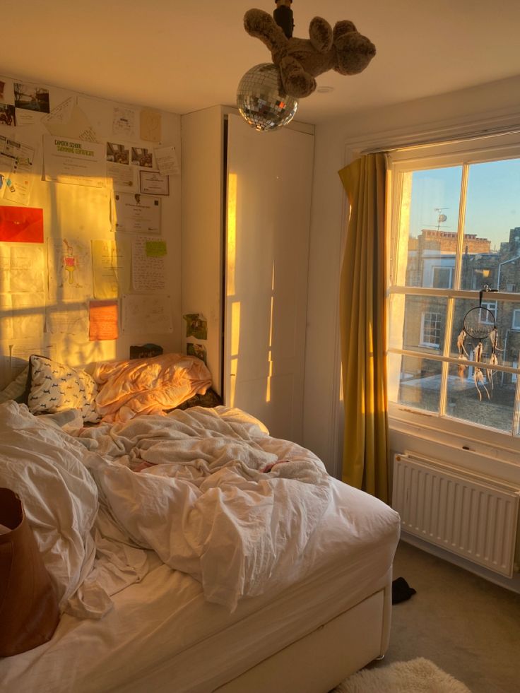 an unmade bed sitting in front of a window next to a wall with pictures on it