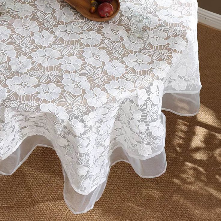 a table topped with a bowl of fruit on top of a lace covered table cloth