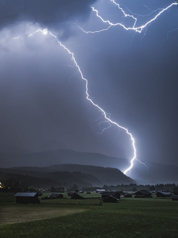 a lightning bolt is seen in the sky over a field with houses and mountains behind it