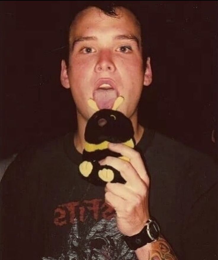 a man holding a stuffed animal up to his mouth while wearing a black t - shirt