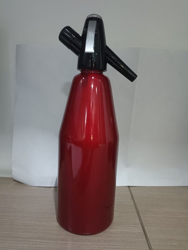 a red plastic bottle with a black top on a tile floor next to a white wall