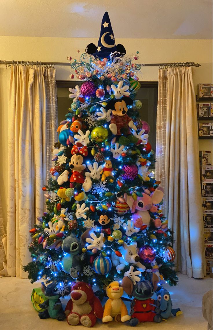 a brightly lit christmas tree in a living room with mickey mouse and friends decorations on it