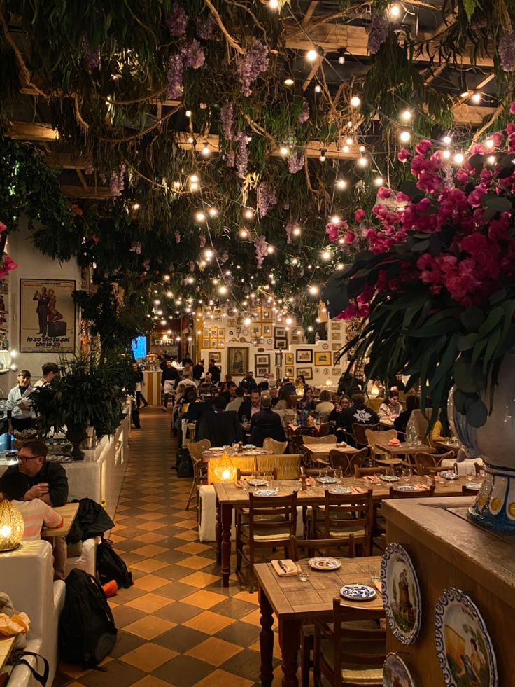 people sitting at tables in a restaurant with lots of lights hanging from the ceiling above them