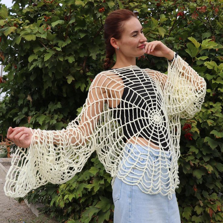 a woman standing in front of some bushes wearing a crochet top and denim shorts