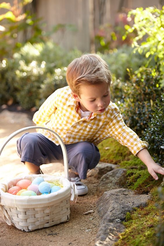 a little boy picking up some eggs from a basket on the ground in front of him