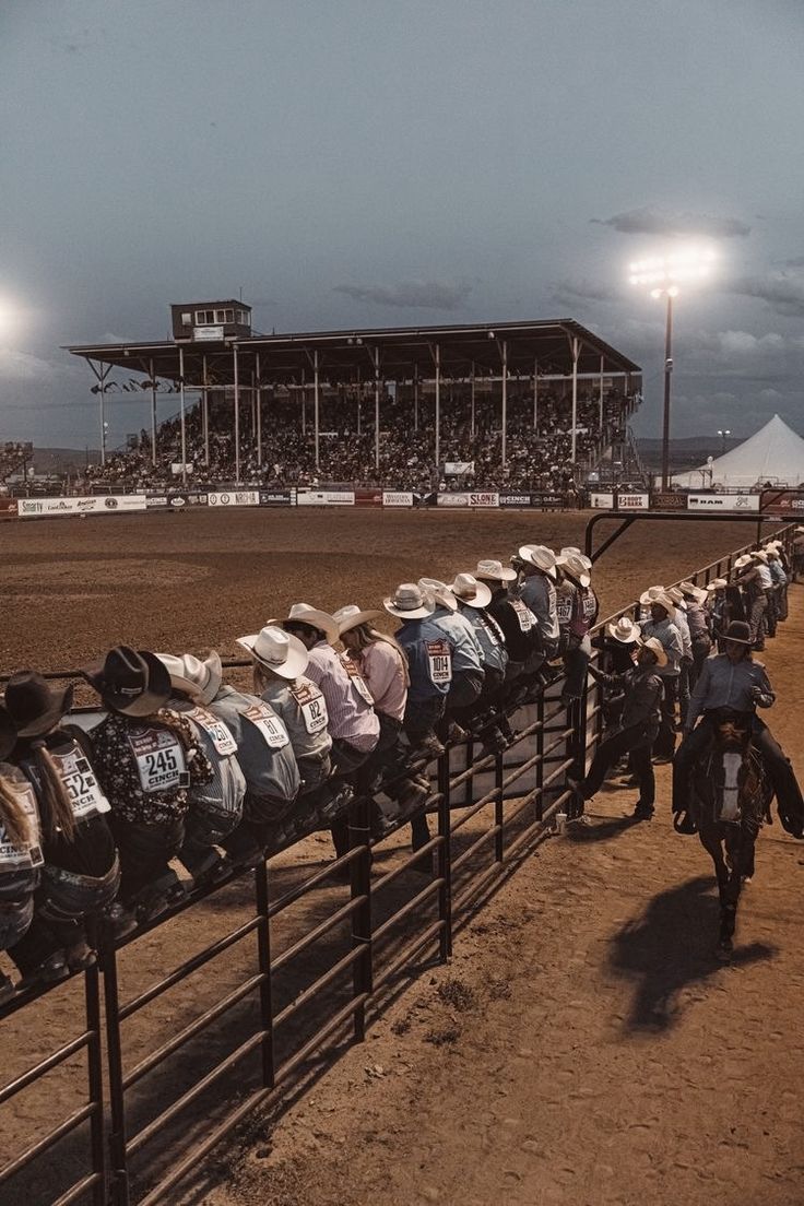 a group of motorcyclists lined up behind a fence at a dirt track