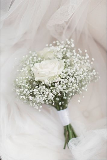 a white bridal bouquet with baby's breath on the bottom is sitting on a bed