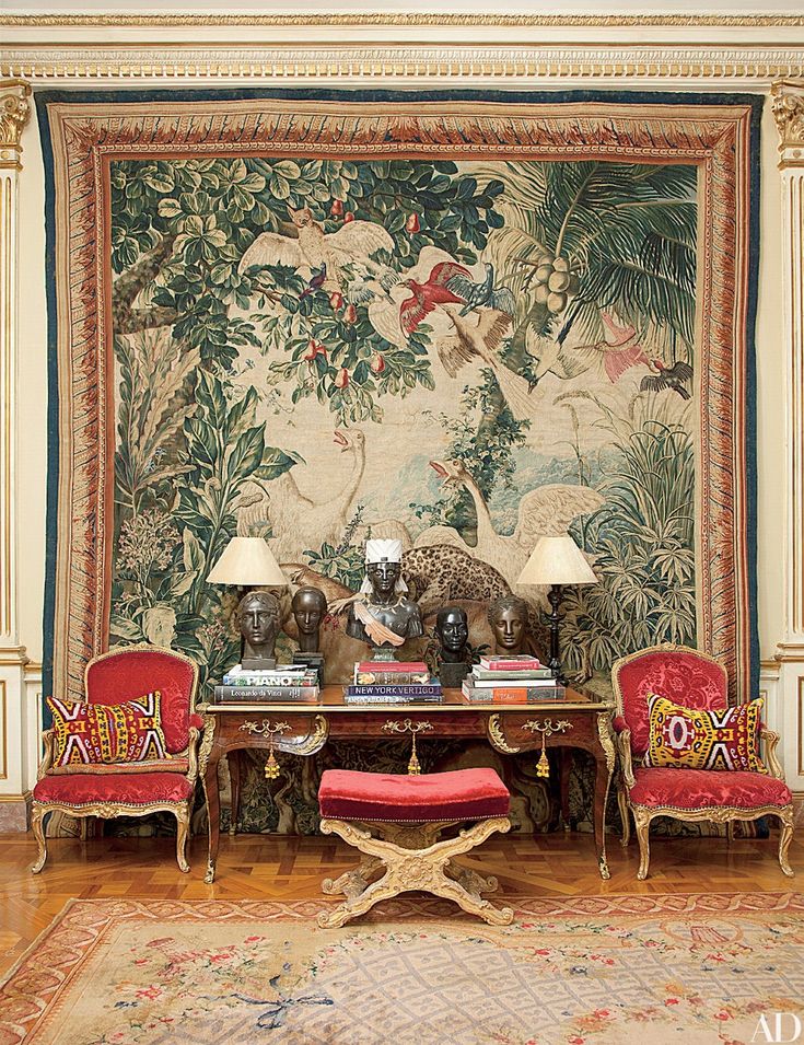 a living room with two red chairs and a tapestry on the wall behind it,