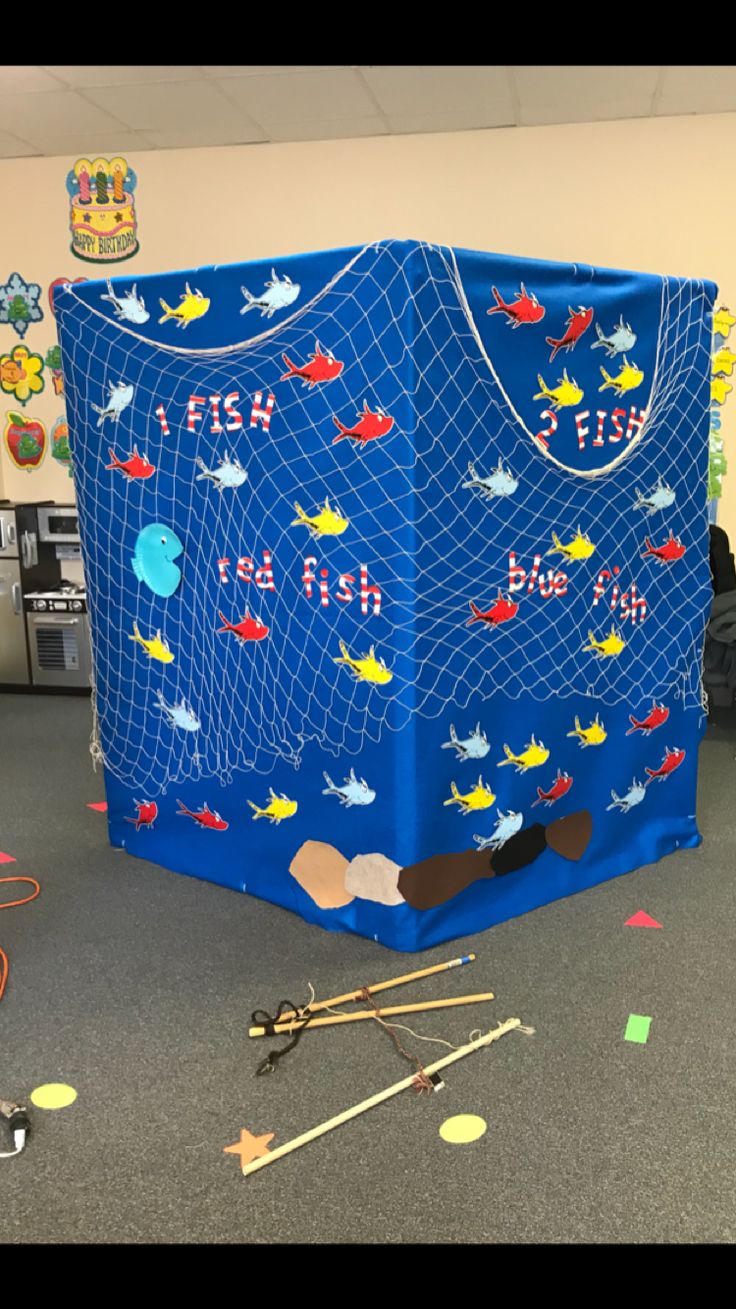 a large blue shopping bag with fish on it in an office cubicle filled with toys