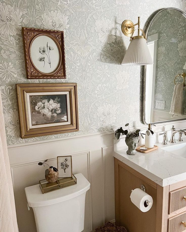 a white toilet sitting under a bathroom mirror next to a wooden sink vanity with two framed pictures on the wall