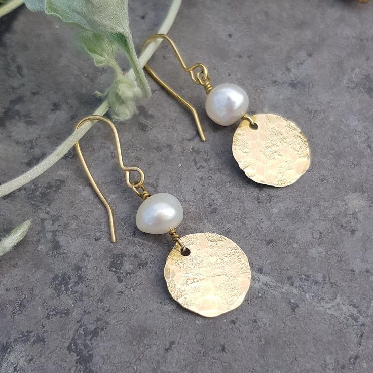 This collection of golden, artisan earrings is made from solid brass and freshwater pearls in beautiful Cornwall. The brass is hand beaten on a weathered, antique anvil, giving a unique and shimmering texture.  This range is inspired by the textures of ancient jewellery, paired with graphic, contemporary shapes. The look is bold and warm, reflecting the Summer sun or bringing a golden glow to grey days. Beaten gold and freshwater pearl was a combination much favoured in Ancient Rome, and it rema Artisan Gold Jewelry With Pearl Charm, Brass Dangle Earrings With Pearl Charm, Dangle Brass Earrings With Pearl Charm, Dangle Earrings With Pearl Charm In Brass, Gold Pearl Earrings With Brass Charm, Handmade Gold Pearl Earrings As A Gift, Handmade Gold Pearl Earrings For Gift, Brass Pearl Earrings As A Gift, Brass Pearl Earrings With Pearl Charm As Gift