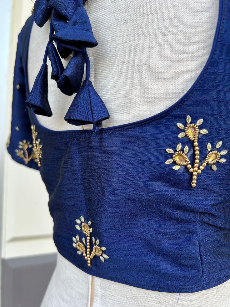 Blue Color Raw Silk Readymade Blouse with beautiful Handwork Work. Item : Readymade BlouseLength of the Blouse : 14 inches Length of the Sleeves : 10 inches Color : Navy BlueBlouse Fabric : Raw SilkLining : Yes, it is fully lined Padded or Non-Padded : PaddedClosure: Front Closure with hooks.Ready-to-Wear : YesDisclaimer - : -This is a Standard Size blouse. We do not guarantee perfect fit as every body and shape is different. Little or no alteration would be required to get the perfect fit. - Co Blue Bohemian Style Blouse Piece For Festive Occasions, Blue Bohemian Blouse Piece For Festive Occasions, Bohemian Blue Silk Blouse Piece, Festive Bohemian Blue Blouse Piece, Blue Bohemian Blouse Piece With Zari Work, Elegant Blue Tops For Festivals, Blue Silk Blouse For Festivals, Blue Silk Blouse With Resham Embroidery, Blue Silk Blouse Piece With Floral Embroidery