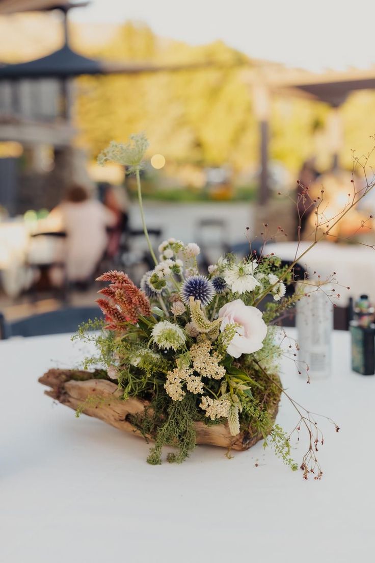 an arrangement of flowers and greenery on a white table cloth at a wedding reception