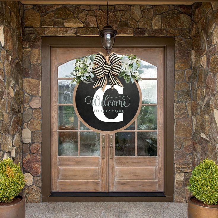 a welcome sign hanging on the front door of a house with two potted plants