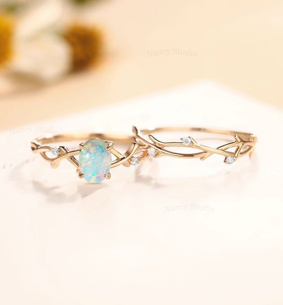 two gold rings with opal and diamonds on top of a white table next to flowers