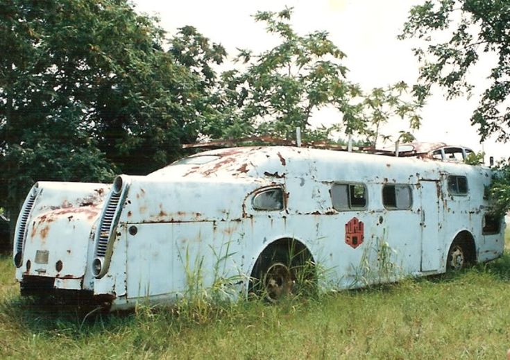 an old bus sitting in the middle of a field with trees and grass around it