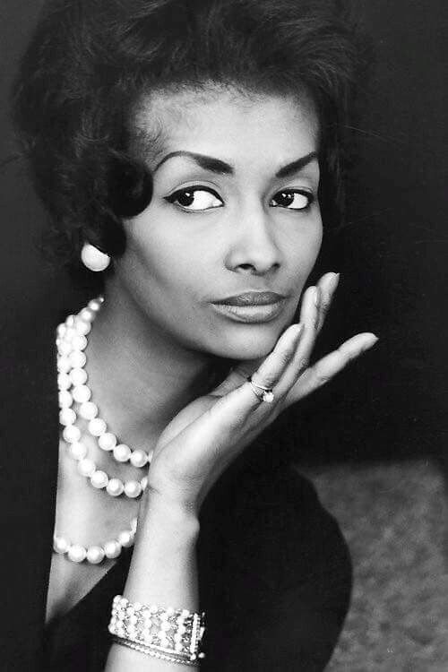 an old black and white photo of a woman with pearls on her necklace, looking at the camera