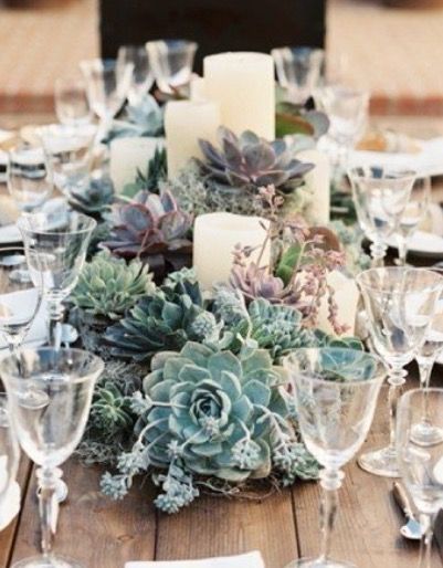 a table topped with lots of glasses and plates covered in succulents next to candles