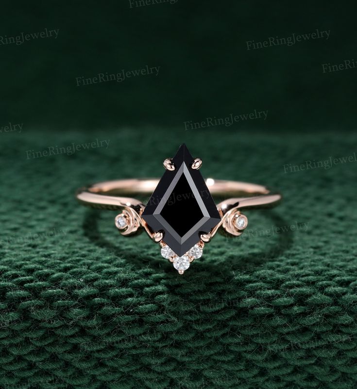 a black diamond ring sitting on top of a green cloth with diamonds around it's edges