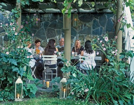 four people sitting at a table in the middle of a garden with plants and flowers