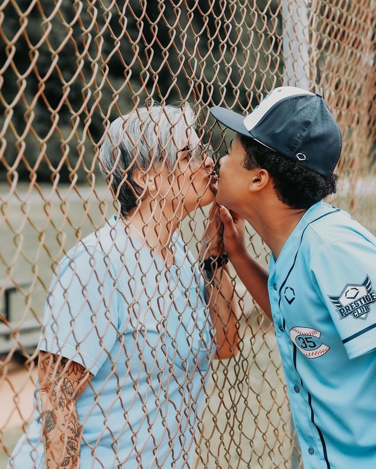 an older man and young boy are kissing behind a chain link fence