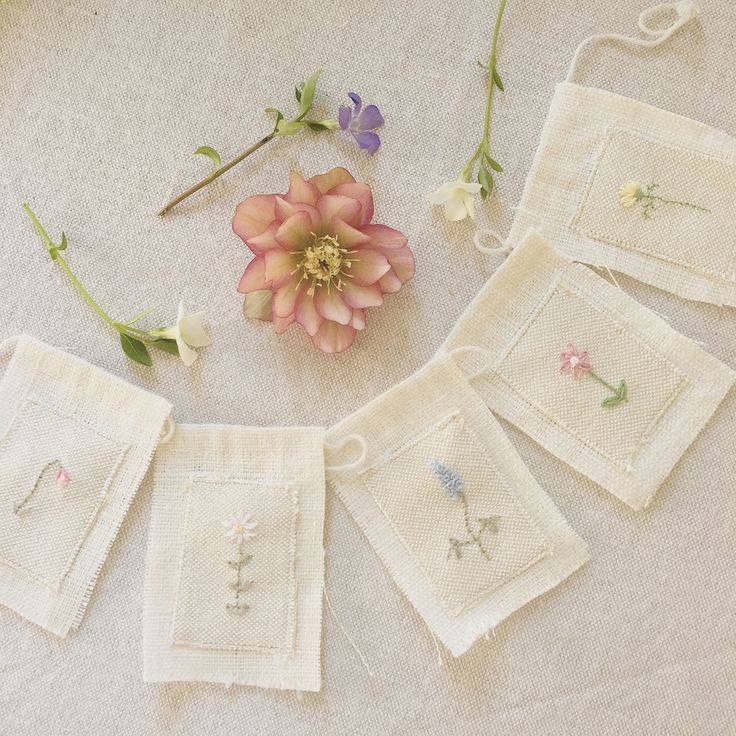 some flowers are sitting on the table with white linens and small embroidered squares around them