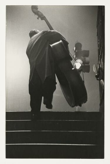 a black and white photo of a man with a cello on the steps in front of him