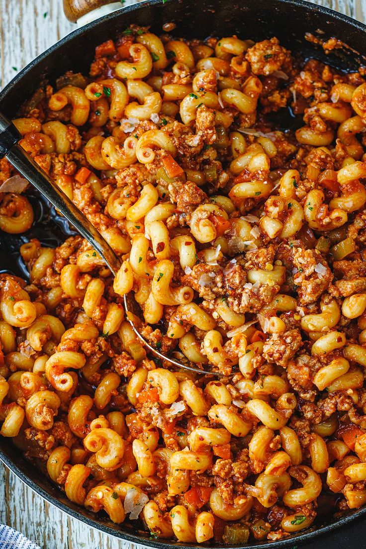 a skillet filled with macaroni and cheese on top of a wooden table