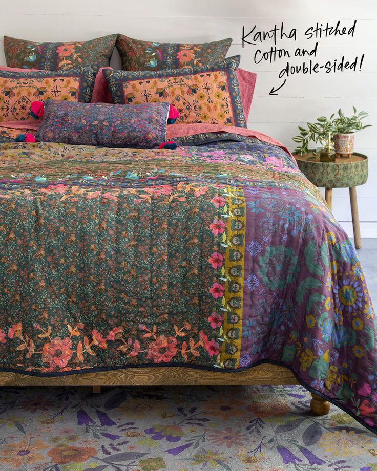 a bed with colorful bedspread and pillows on it in a room next to a table