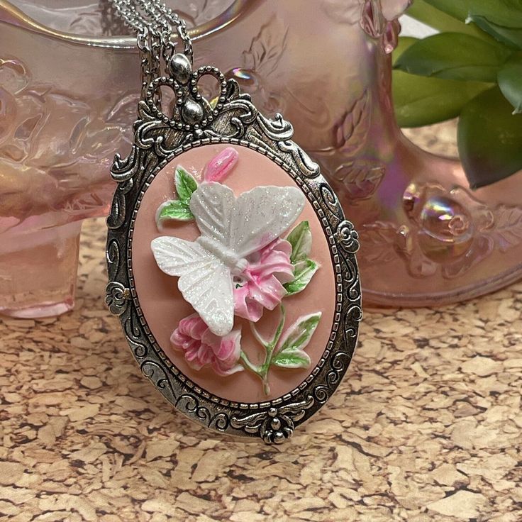 Add a touch of elegance to your outfit with this stunning 3D butterfly cameo pendant necklace. The oval-shaped pendant features a beautiful butterfly perched on a flower, with a pink main stone and nonexistent secondary stone. The pendant is made of resin and crafted with Tibetan silver, with an antique bronze and white gold finish that gives it a unique and sophisticated look.  This necklace is perfect for any occasion, especially birthdays, and makes a great gift for females who appreciate Victorian style jewelry. The necklace is 24 inches long and comes with a charm pendant/locket type, making it a great addition to any collection. The butterfly on flower theme adds a touch of whimsy and elegance to any outfit. Antique Cameo Jewelry, Pink Pendant Necklace, Faceted Glass Bead Necklace, Butterfly On Flower, Victorian Style Jewelry, Pink Pendant, Cameo Pendant Necklace, Style Birthday, 3d Rose