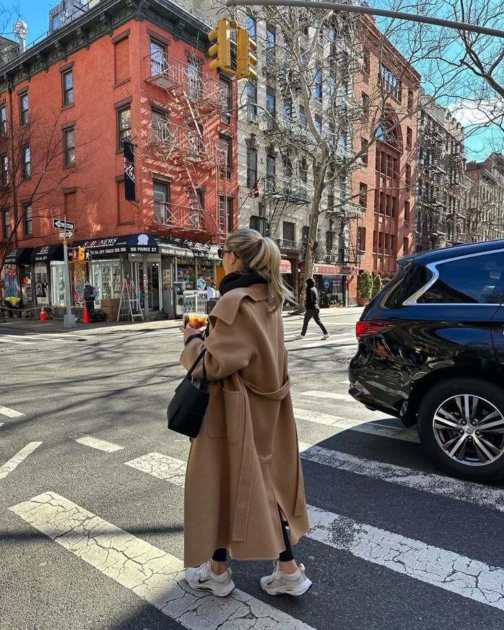 a woman in a trench coat is crossing the street