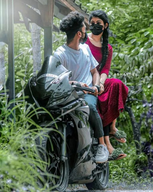 a man and woman riding on the back of a motorcycle next to lush green trees