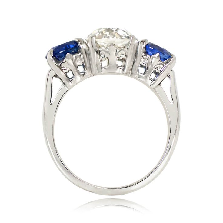 This antique three-stone engagement ring centers a 2.04 carat old European cut diamond, J color and VS1 clarity, set in prongs. The diamond is accented by two round cut sapphires with a combined weight of 2.56 carats, also set in prongs. The handcrafted platinum mounting features a fleur-de-lis motif on the under-gallery. This ring is from the Art Deco era, circa 1930.
The old European diamond measures approximately 7.83mm x 7.78mm x 5.19mm. The sapphires measure approximately 6.31mm x 6.16mm x Three Stone Sapphire Round Ring Fine Jewelry, Heirloom Sapphire Three Stone Ring, Heirloom Three Stone Sapphire Ring, Heirloom Sapphire Ring With Three Stones, Timeless Round Three Stone Sapphire Ring, Luxury Three Stone Round Cut Sapphire Ring, Anniversary Three-stone Diamond Sapphire Ring, Art Deco Three Stone Diamond Ring, Three Stone Lab-created Sapphire Diamond Ring