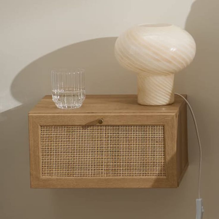 a white vase sitting on top of a wooden cabinet next to a glass filled with water