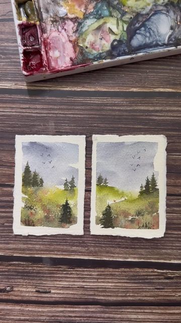 two small paintings are sitting on a wooden table next to a brush and watercolor palette