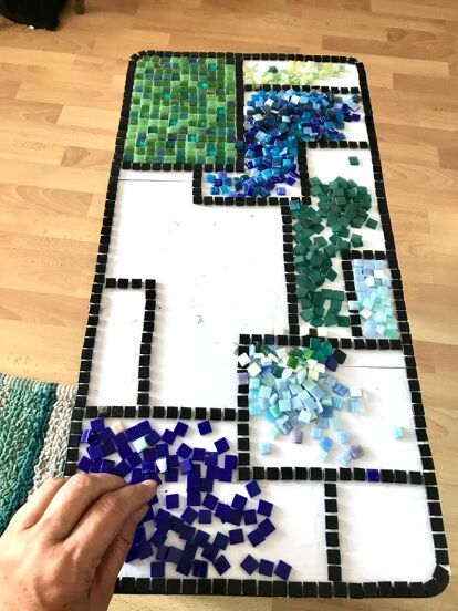 someone is making a mosaic table top with blue, green and white tiles on it