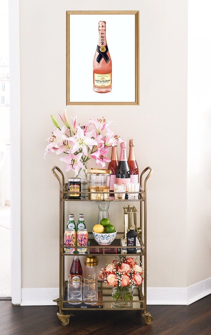 a bar cart filled with bottles and flowers on top of a hard wood floor next to a white wall