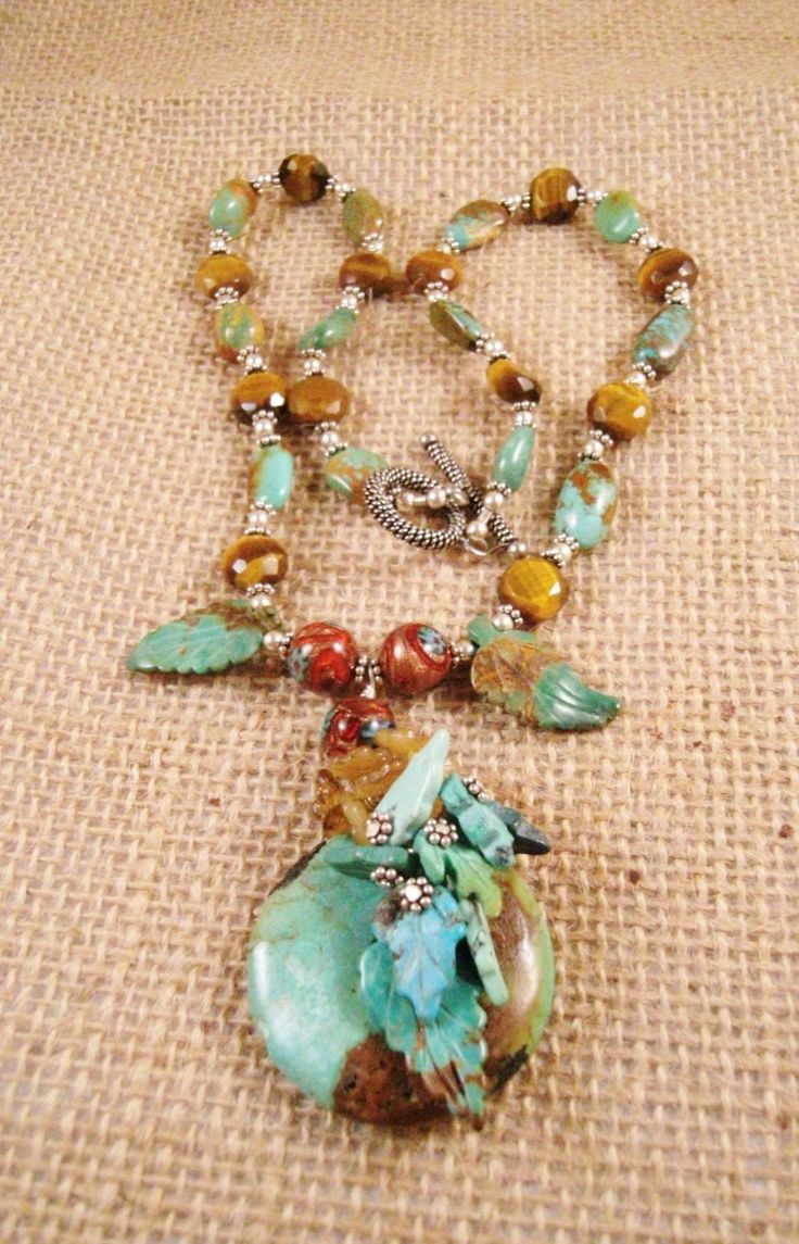 This elegant, statement necklace will remind you of when the leaves start to turn colors in the autumn.  The centerpiece is a beautiful turquoise doughnut with flecks of brown.  It was embellished with genuine turquoise carved leaves, glass flowers and sterling silver.  The necklace hangs 11 inches long, the centerpiece is 3 1/2 inches wide.  The strap has genuine turquoise, sterling silver, and tiger eye beads, with a beautiful toggle clasp, of sterling silver.  It can be worn on any occasion, to embellish a business outfit, or casual outfit.  All gemstones are high quality and genuine.  It can be passed down as an heirloom for generations to come, as it is constructed of high quality materials. Nature-inspired Turquoise Gemstone Beads Jewelry, Turquoise Beaded Nature-inspired Jewelry, Nature-inspired Beaded Turquoise Jewelry, Nature-inspired Turquoise Beaded Jewelry, Handmade Turquoise Beaded Necklace Nature-inspired, Handmade Turquoise Beaded Necklaces Nature-inspired, Handmade Turquoise Beaded Necklace, Nature-inspired, Unique Turquoise Necklace With Polished Beads, Elegant Statement Necklace