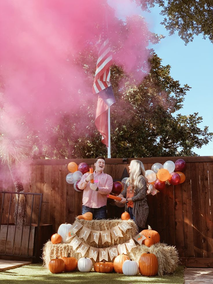 two people standing in front of a table with balloons and pumpkins on the ground