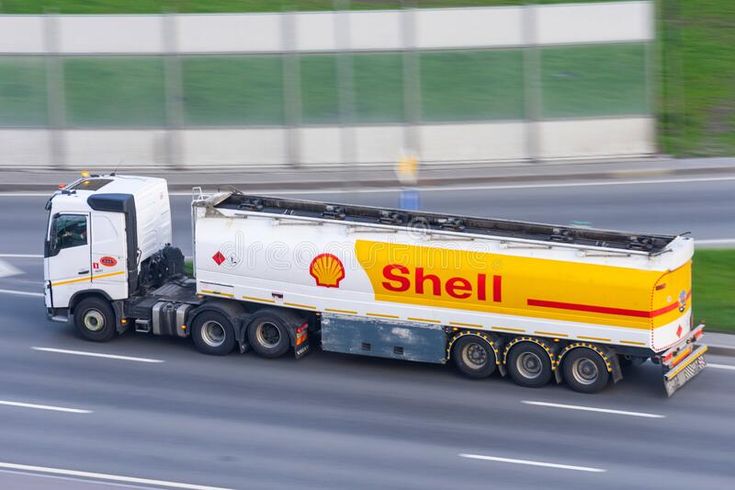 a white and yellow shell truck driving down the road with grass in the back ground