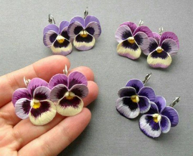 a hand is holding four small purple and white pansyflowers, one being held in front of the other