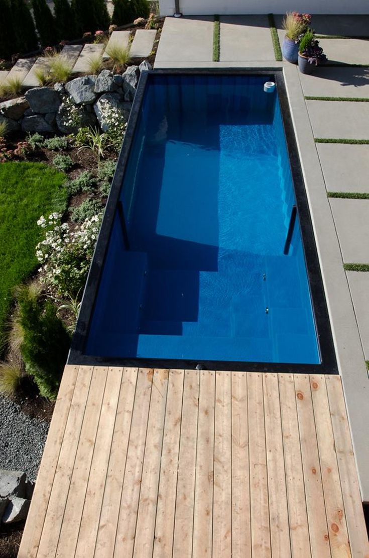 an above ground swimming pool with wooden decking next to grass and flowers in the background