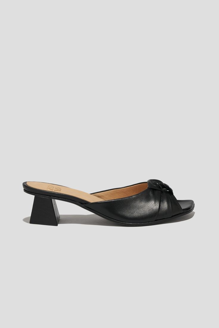 The Greta is a boudoir slipper-inspired mule that captures a playful mix of daytime sensibility & evening refinement. Whether you’re wearing Greta for daytime play or after-dark doings, you will feel both comfortable and well-turned-out, thanks to a low, triangular heel and a pretty pleated-knot detail at the toe. Style Greta back to loose, casual pants for a breezy date look, or wear them with a cocktail dress to the next wedding on your calendar. Kidskin leather upper, vegetable tanned leather lining, leather outsole. Heel height: 1 ¾ inches (45 mm) Handmade in Argentina Chic Sandals With Almond Toe For Gala, Chic Almond Toe Sandals For Galas, Chic Almond Toe Sandals For Gala, Evening Slip-on Heels With Sculpted Heel, Elegant Slip-on Sandals With Sculpted Heel, Chic Evening Slip-on Sandals, Elegant Summer Slip-on Kitten Heels, Chic Mules With Padded Heel For Cocktail, Chic Open Heel Kitten Heels For Evening