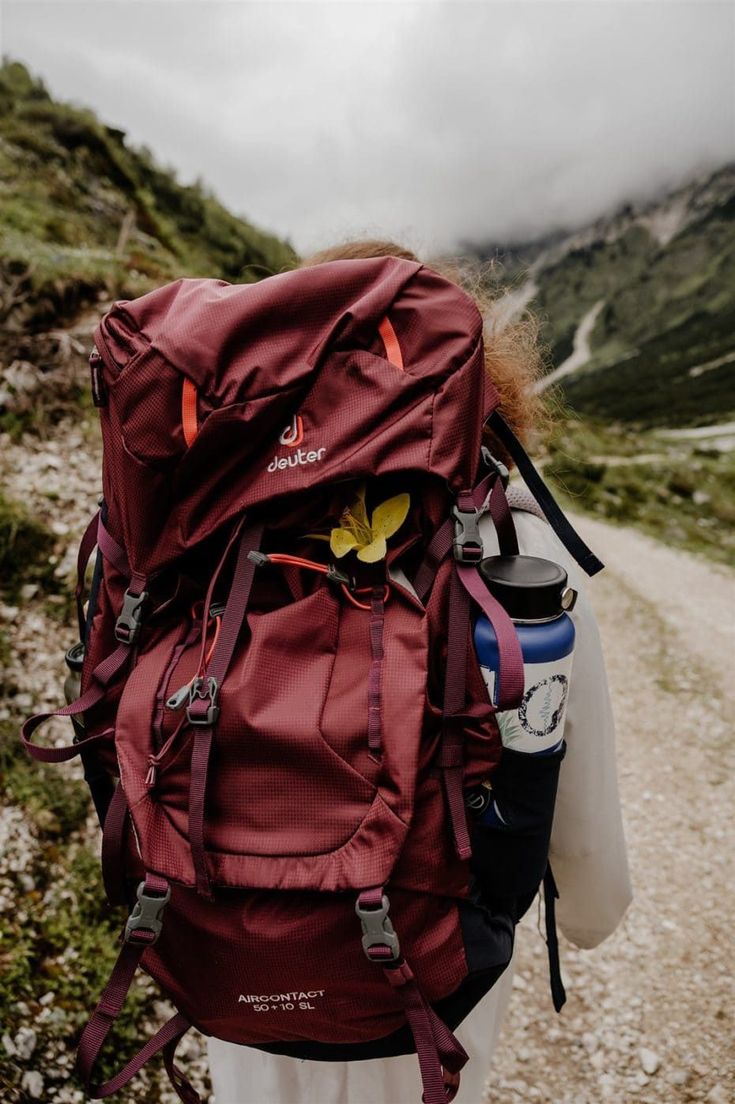 a person with a large backpack on their back walking up a dirt road in the mountains