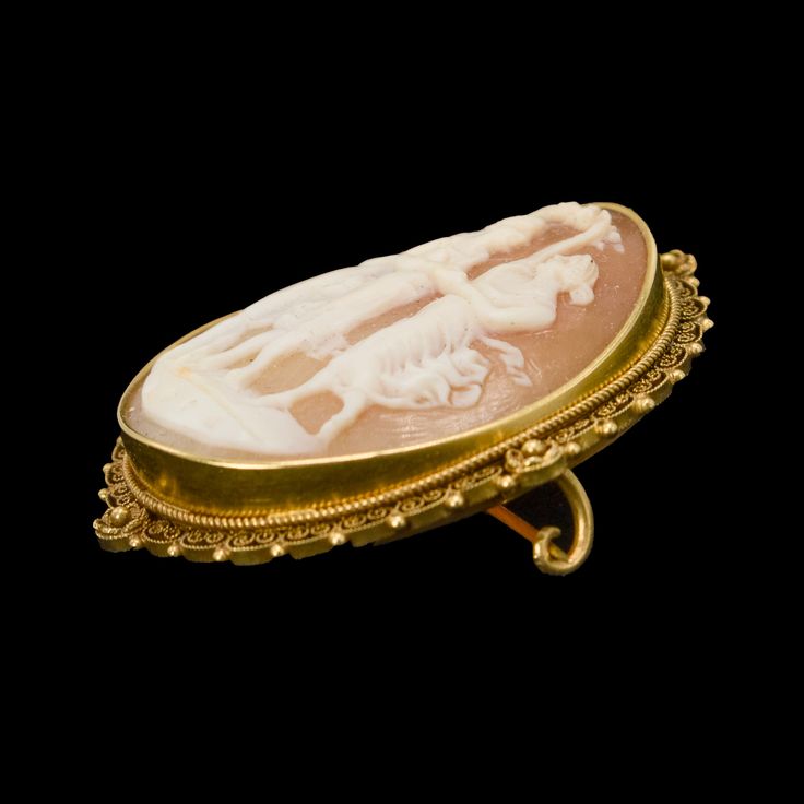 In the 19th century, a slew of archaeological discoveries in Italy spawned a renewed interest in classical history — including jewelry! This style is called "Etruscan Revival," named for Etruria, an ancient civilization near Rome that predated its founding and influenced its culture. This cameo is made of shell and features an ornate carving of the Three Graces, daughters of Zeus who bestowed what is most pleasurable and beneficent in nature and society: Euphrosyne (mirth), Aglaia (elegance) and Historical Yellow Gold Jewelry For Ceremonial Use, Historical Yellow Gold Jewelry For Ceremonies, Historical Yellow Gold Jewelry For Ceremonial Occasions, Historical Ceremonial Yellow Gold Jewelry, Ancient Style Yellow Gold Ceremonial Jewelry, Ancient Yellow Gold Jewelry For Ceremonial Occasions, Ancient Style Yellow Gold Jewelry For Ceremonial Occasions, Historical Yellow Gold Engraved Jewelry, Collectible Ancient Style Yellow Gold Jewelry